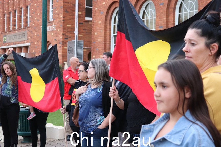妇女们站在红砖建筑前，举着原住民旗帜