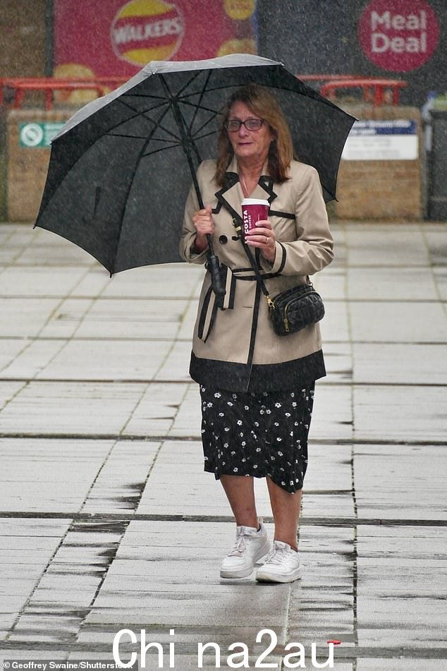 一位女士在雷丁车站附近面临倾盆大雨,拿起咖啡勇敢走上街头