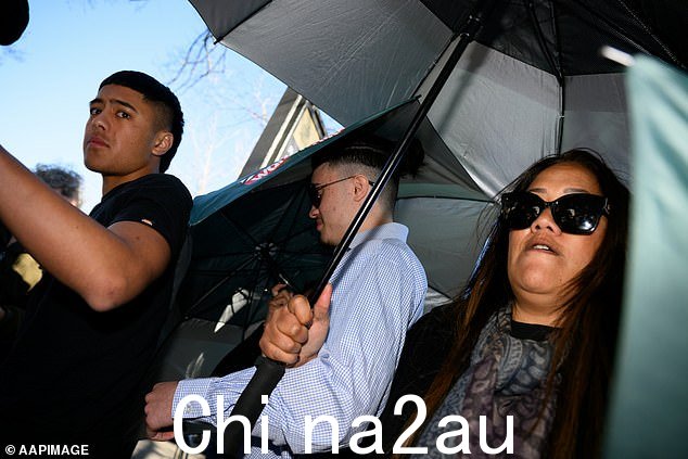 爱德华兹的家人和朋友撑起雨伞,试图遮住少年的脸