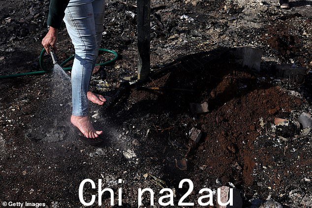 一位不愿透露姓名的居民在邻居家踩过滚烫的余烬后,用花园软管给脚降温。被摧毁