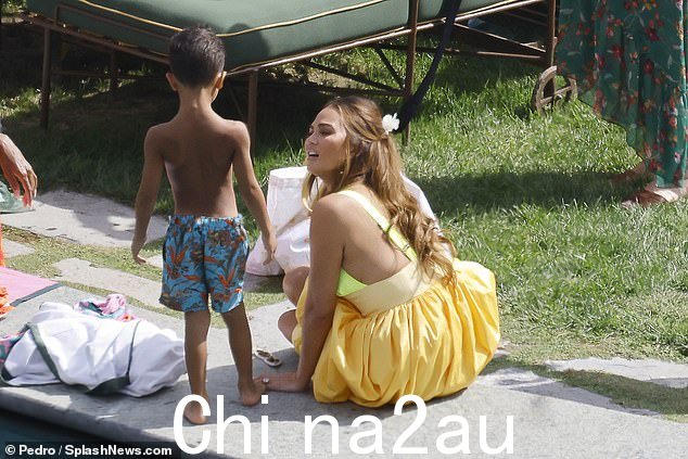 背心裙:Chrissy 穿着一件可爱的背心裙,有两种黄色。上衣的剪裁像泳衣上衣,是亮黄色,而宽松的裙子是玉米色