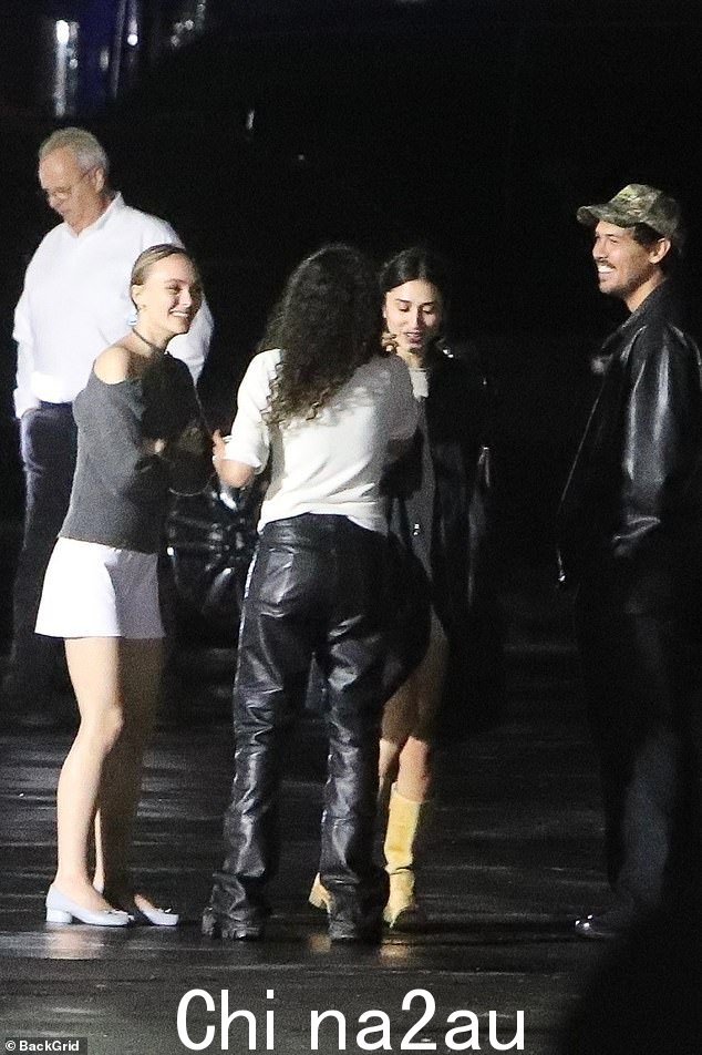 莉莉-罗丝·德普 (Lily-Rose Depp) 身穿灰色上衣和白色裙子,在演出中与朋友聊天时微笑着