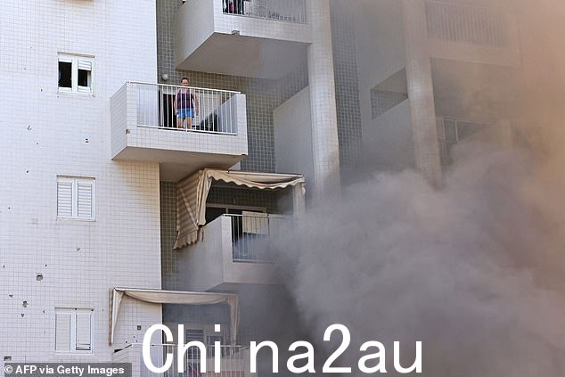 以色列南部城市阿什凯隆遭受来自加沙地带的火箭袭击后,一名妇女站在阳台上,一栋住宅楼的停车场冒出滚滚浓烟