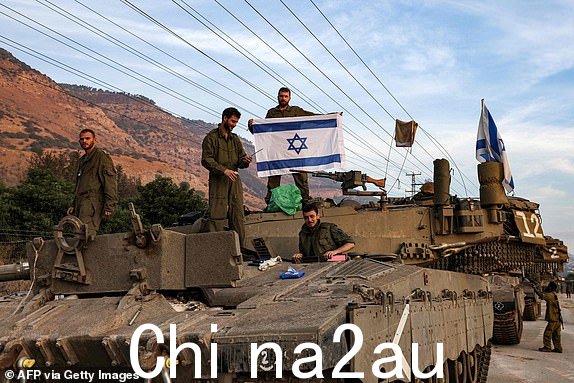 一名以色列士兵伸展身体2023 年 10 月 11 日，在以色列北部靠近黎巴嫩边境的上加利利地区，一列坦克聚集在梅卡瓦主战坦克的炮塔顶上，以色列国旗飘扬。（摄影：Jalaa MAREY / 法新社）（摄影：JALAA MAREY/法新社（来自 Getty Images）