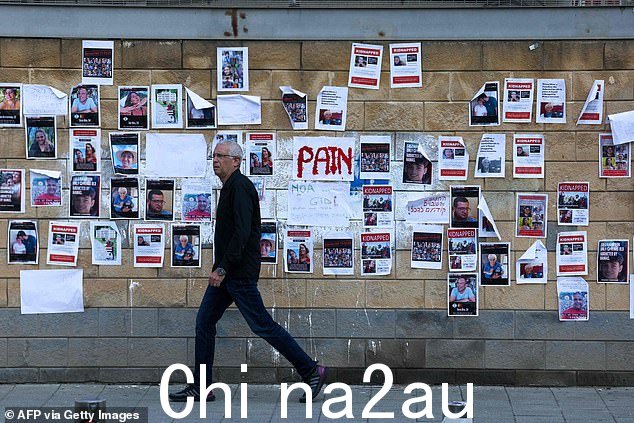 2023 年 10 月 16 日特拉维夫国防部外的墙上贴着上周巴勒斯坦武装组织哈马斯突然袭击以色列时劫持的以色列人质的照片,一名男子走过