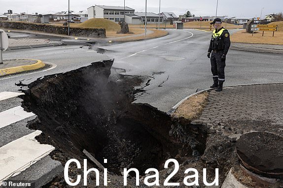 2023 年 11 月 15 日，冰岛格林达维克渔镇因火山活动而疏散，一名警察站在路缝旁。REUTERS/Marko Djurica