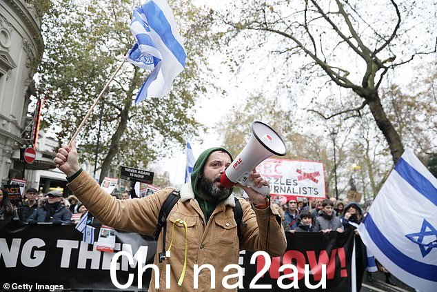 周日游行中一名示威者一边挥舞着以色列国旗一边对着麦克风讲话