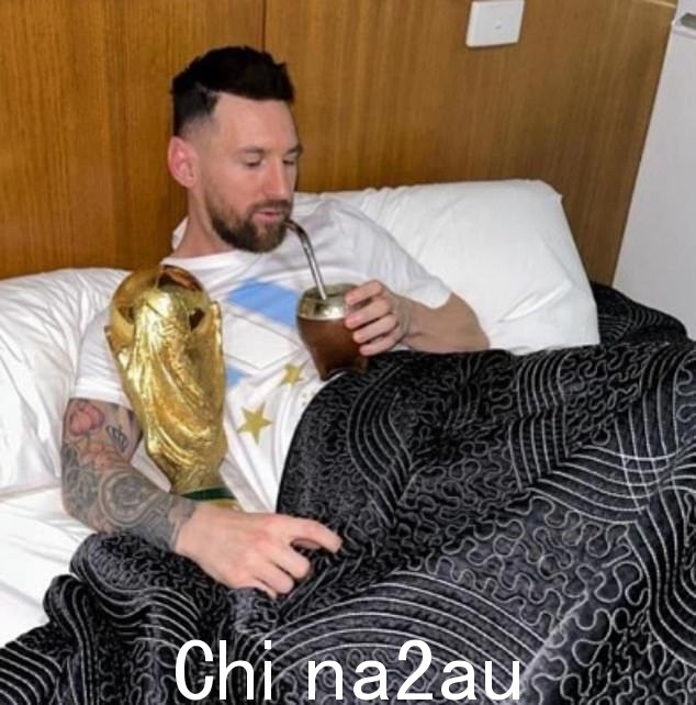梅西坐在床上,腋下夹着世界杯奖杯,手里拿着伴侣葫芦