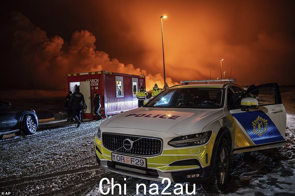周一晚上,警车停在冰岛雷克雅内斯半岛格林达维克附近通往格林达瓦克的公路入口处,以火山喷发为背景