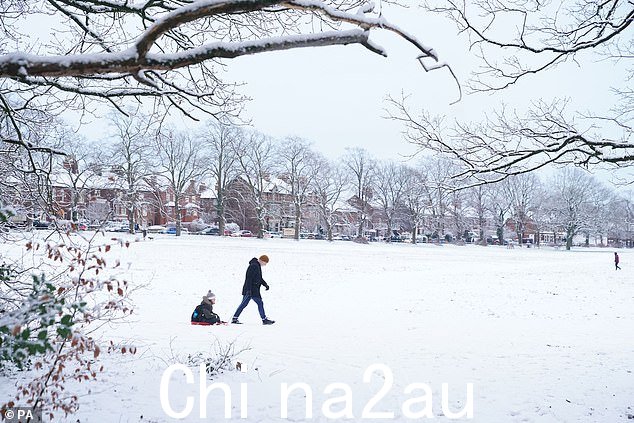柴郡:一个人在纳茨福德希思 (Knutsford Heath) 的雪地上拉着雪橇上的孩子
