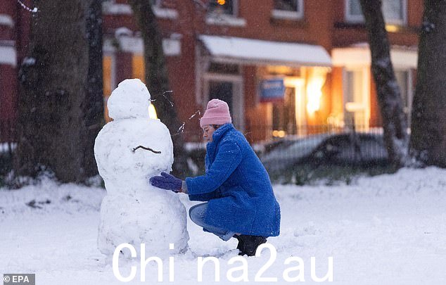 利物浦:一位戴着粉色羊毛帽子和蓝色外套的女人在 Greenbank 公园堆雪人