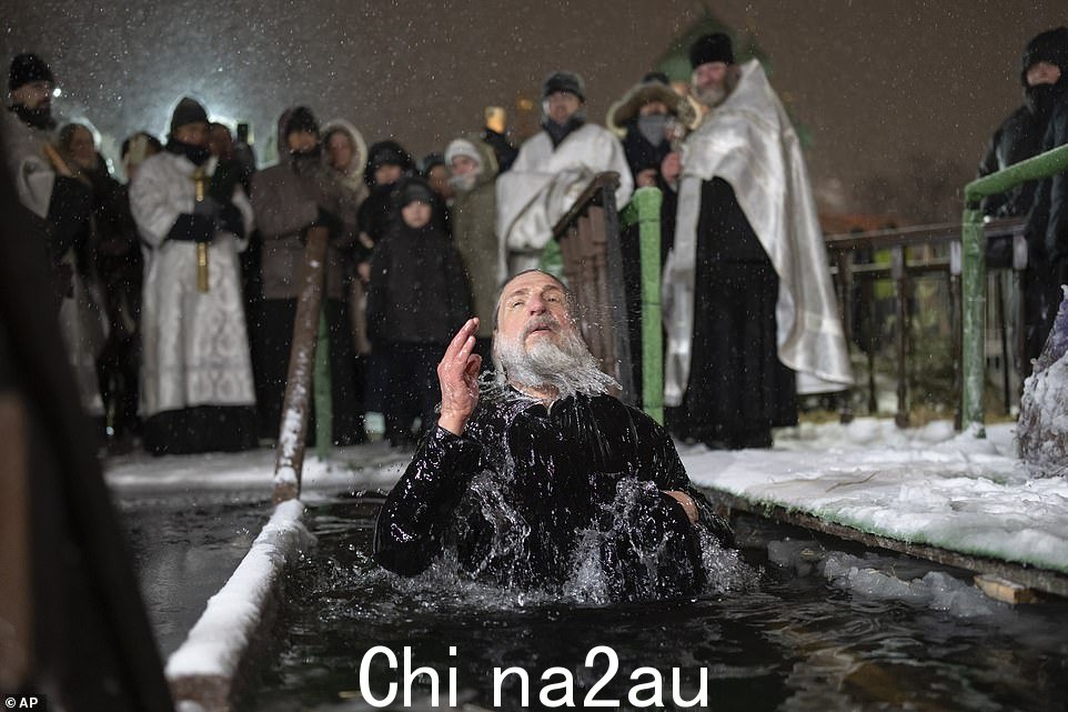 俄罗斯东正教牧师在主显节的冰水中沐浴时画十字,在莫斯科大宫殿池塘举行传统的主显节,背景是奥斯坦金诺的圣三一教堂俄罗斯,星期四