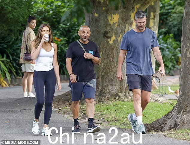Nadia 拿着外卖咖啡,在穿过郊区公园时与 Peter 和另一位男性朋友(中)聊天