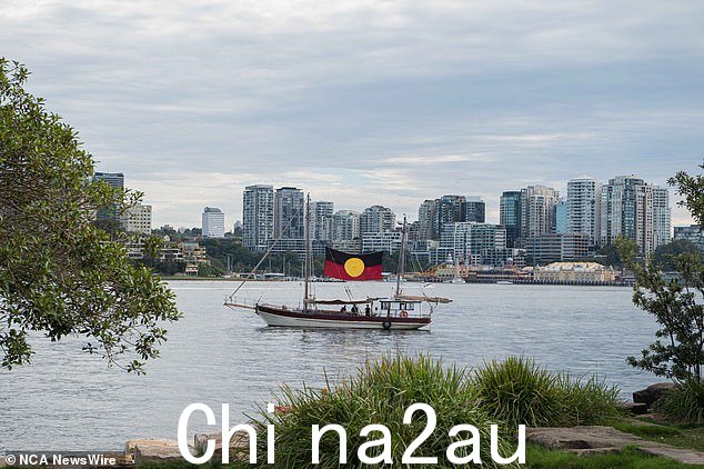 在水面上,一艘悬挂原住民旗帜的老式船驶过 237 年前第一舰队抵达的港口