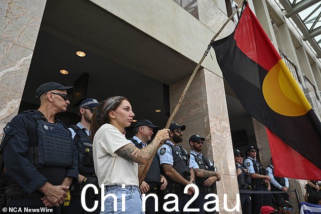 一名活动人士在议会大厦外挥舞着原住民旗帜,警察在后面监视