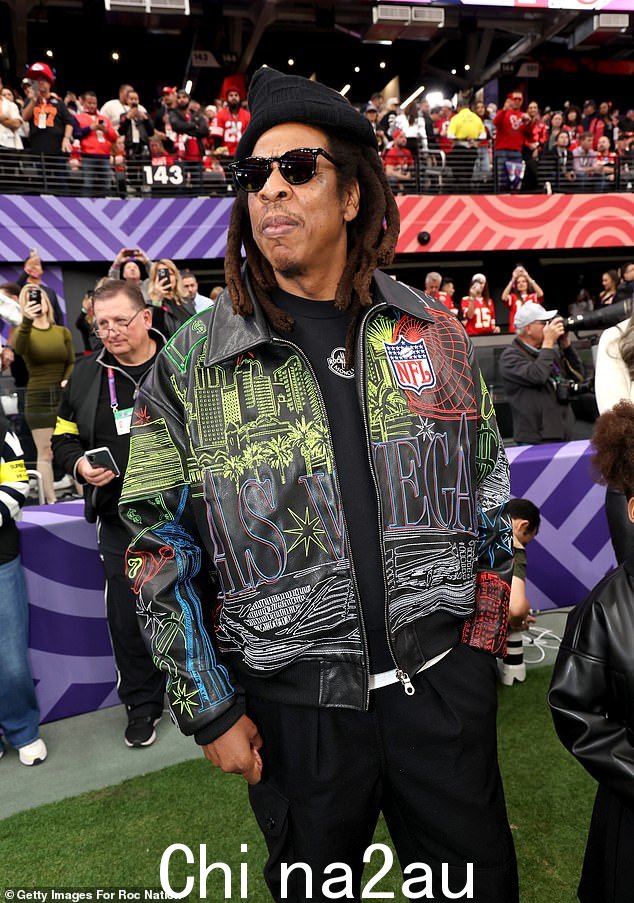 Jay-Z 在黑色上衣外穿一件带图案的黑色夹克,搭配黑色裤子、针织帽和太阳镜