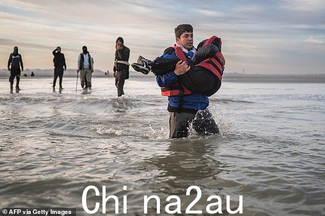 2022 年 10 月 12 日,法国北部敦刻尔克附近的格拉沃利讷海滩,一名移民背着一个孩子,身后跟着走私犯,准备登上走私犯的船