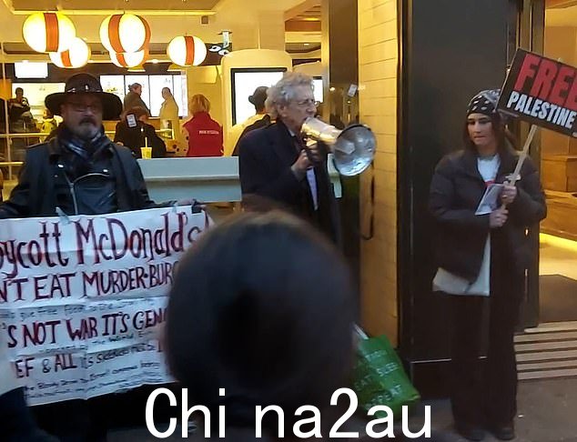 这位 76 岁的反疫苗活动人士两侧是另外两名示威者,他们举着写有“自由巴勒斯坦”和“抵制麦当劳!”的标语。不要吃谋杀汉堡'