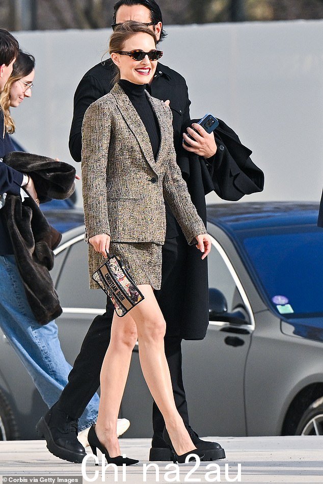《名利场》杂志封面女郎在 2 月 27 日巴黎时装周上的 Christian Dior 2024-2025 秋冬女装秀上微笑着向粉丝们挥手致意。这位 5 月 12 月的女演员身穿花呢西装外套身穿黑色高领毛衣和迷你裙,搭配墨镜和细高跟鞋,手拿一个印有设计师名字的小手拿包。” class=