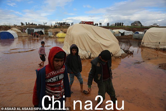 2023 年 3 月 19 日一场暴雨袭击叙利亚东北部部分地区后,男孩们涉水穿过被洪水淹没的 Roj 营地