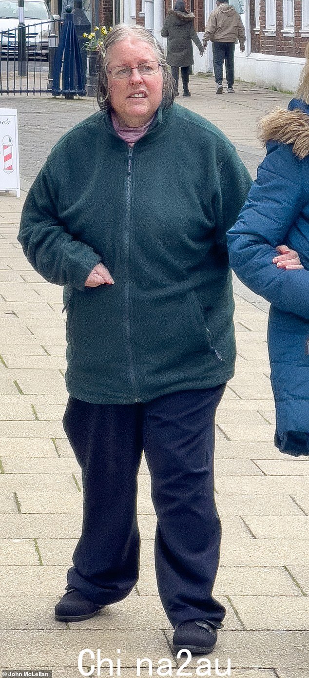 她在剑桥郡亨廷顿市中心漫步时穿着深绿色羊毛衫、海军蓝裤子和眼镜