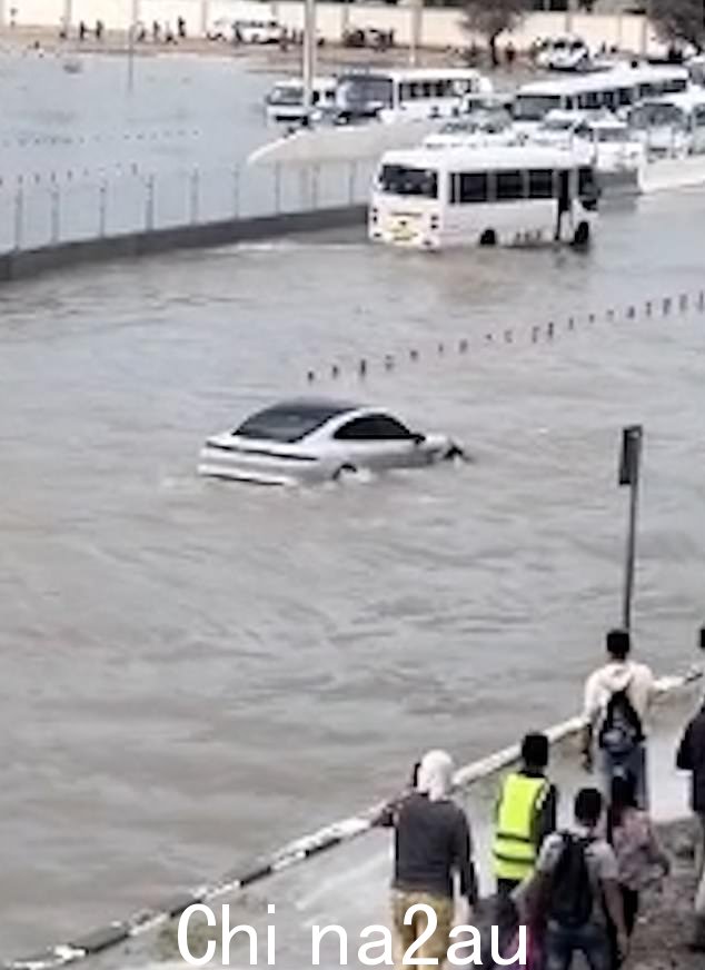 一辆保时捷在被洪水淹没的道路上漂流,旁观者震惊地看着