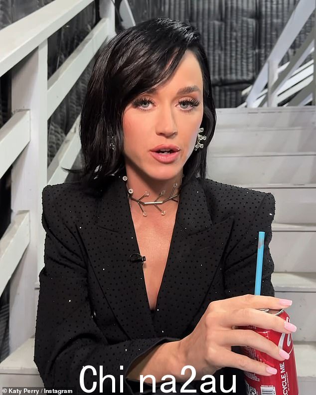 这位女歌手穿着闪闪发光的黑色西装迷你裙,搭配银色耳环和高跟鞋,喝着一罐可口可乐,展现出迷人的身材