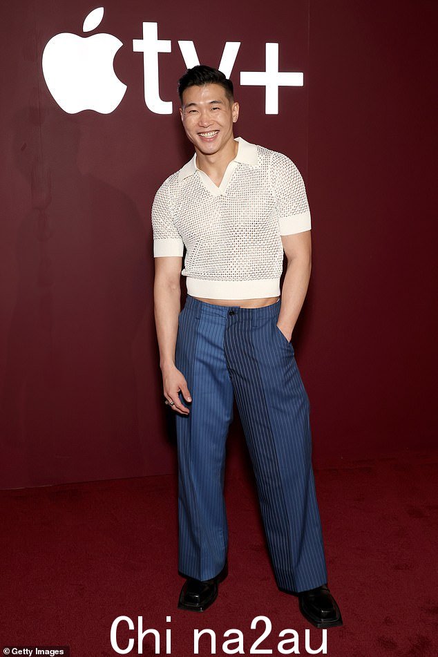 Joel Kim Booster 穿着网眼 Polo 衫和蓝色细条纹裤子,看上去肌肉发达。