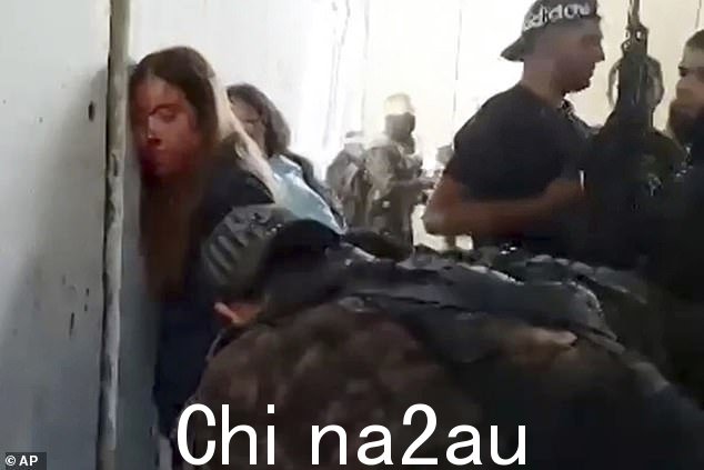 来自纳哈尔奥兹军事基地的以色列女兵在 2023 年 10 月 7 日被哈马斯成员俘虏后,被放在墙边并戴上镣铐