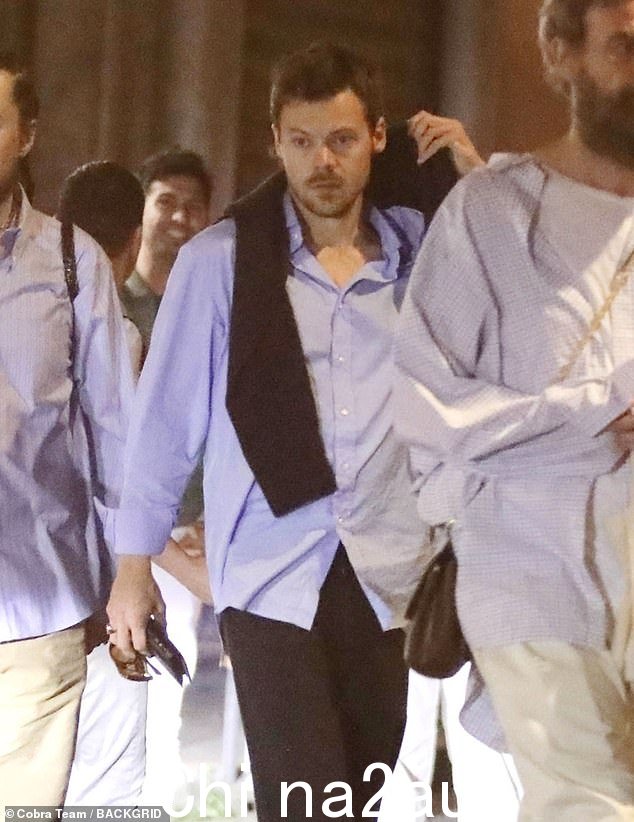 他穿着一件宽松的时尚服装,穿着一件超大的蓝色纽扣衬衫,没有塞进一条黑色裤子,看起来很英俊