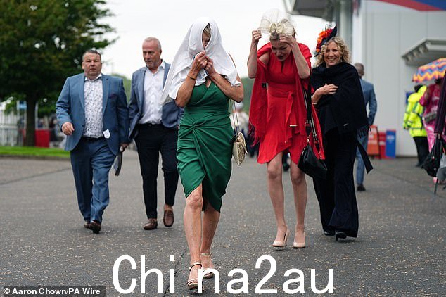 周五抵达萨里埃普索姆赛马场参加德比赛马节的赛马爱好者穿着夹克和外套避雨