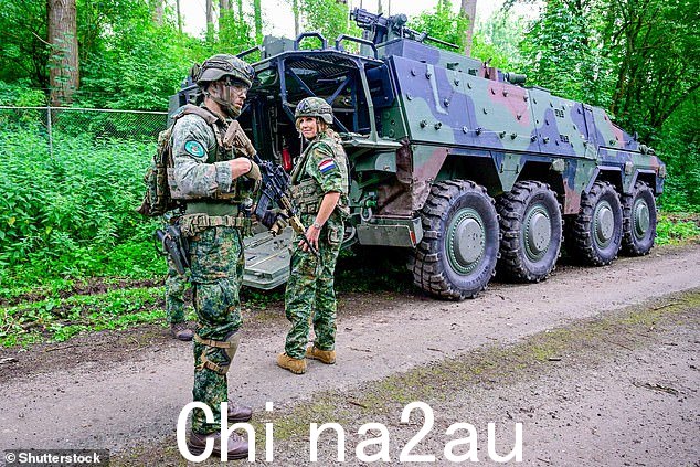 女王站在一名持枪士兵旁边。女王并没有被激烈的环境吓倒