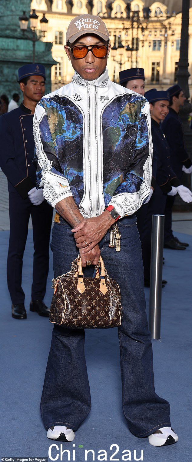 Pharrell Williams 选择深色喇叭牛仔裤搭配白色运动鞋、Louis Vuitton 包和阿特拉斯印花夹克