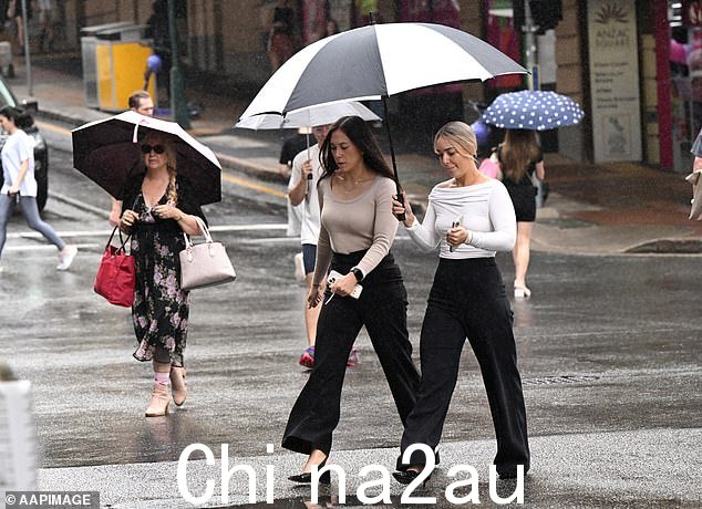 未来几天,澳大利亚大片地区将面临一年的降雨量,增加洪水以及道路和铁路关闭的风险。图中为撑伞的妇女