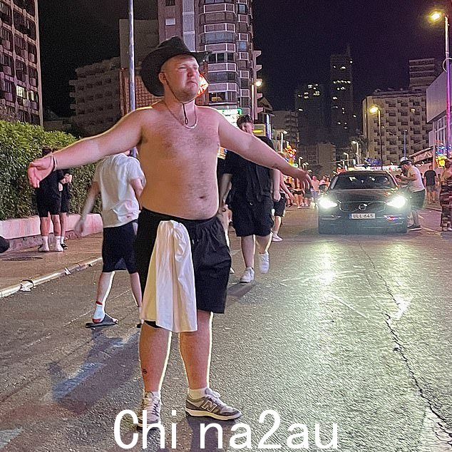一名英国游客将衬衫塞进黑色短裤,赤裸上身站在路中央