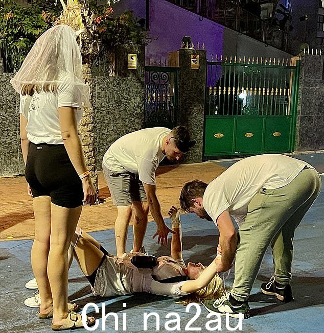 一个戴着新娘面纱的女人看着她的朋友被两个男人扶起来