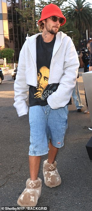 他穿着黑色 Bob Marley T 恤和腰部抽绳酸洗牛仔裤短裤
