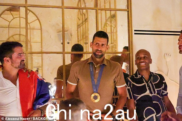 Novak 在餐厅内穿着棕色 Polo 上衣、棕褐色裤子和白色运动鞋,周围都是朋友