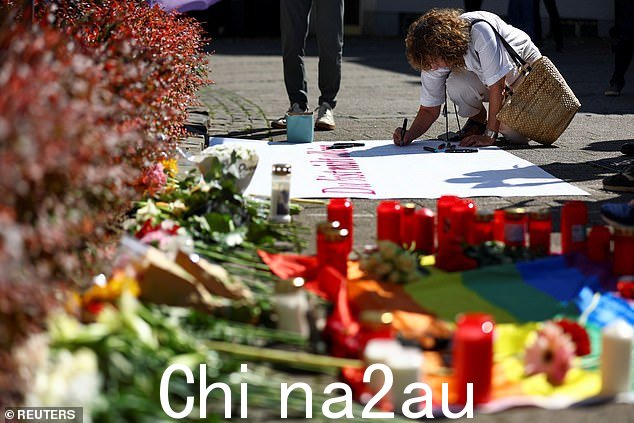 攻击后,一名妇女在地上的致敬物品附近的标语牌上写字