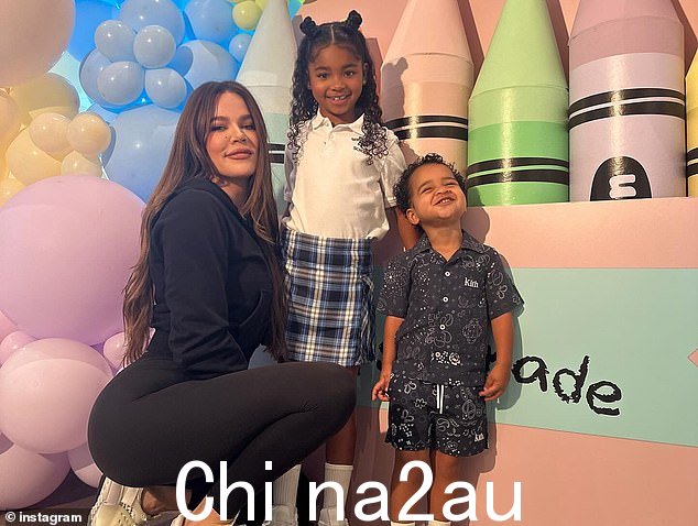 Khloe 甜蜜地拥抱了她的女儿 - 她抱着家里的猫 - 他们都在一块写着“一年级第一天”的牌子前摆姿势,背景是巨大的蜡笔和彩色气球