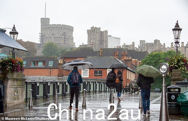 通勤者在倾盆大雨中行走,背景是温莎城堡