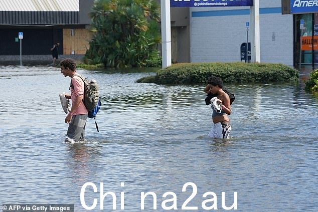 米尔顿淹没城市后,周四下午,两个人走过坦帕被洪水淹没的街道