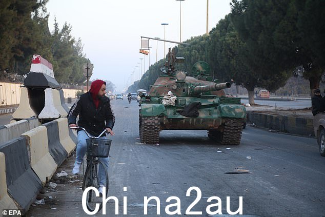 旁边有一个人坐在自行车上12 月 8 日,叙利亚霍姆斯的一辆坦克